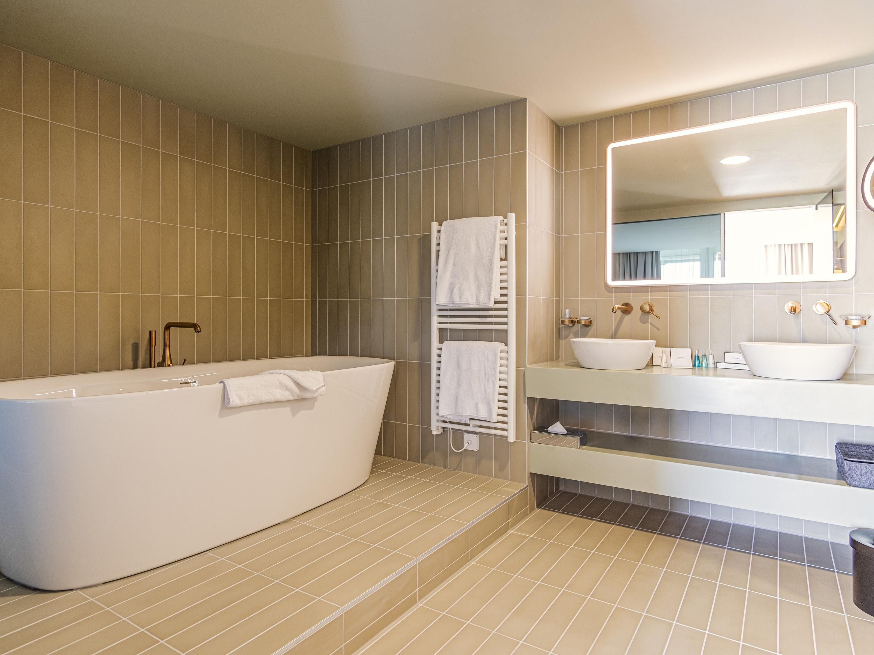 Un baño moderno con una bañera independiente, un espejo grande y dos lavamanos.