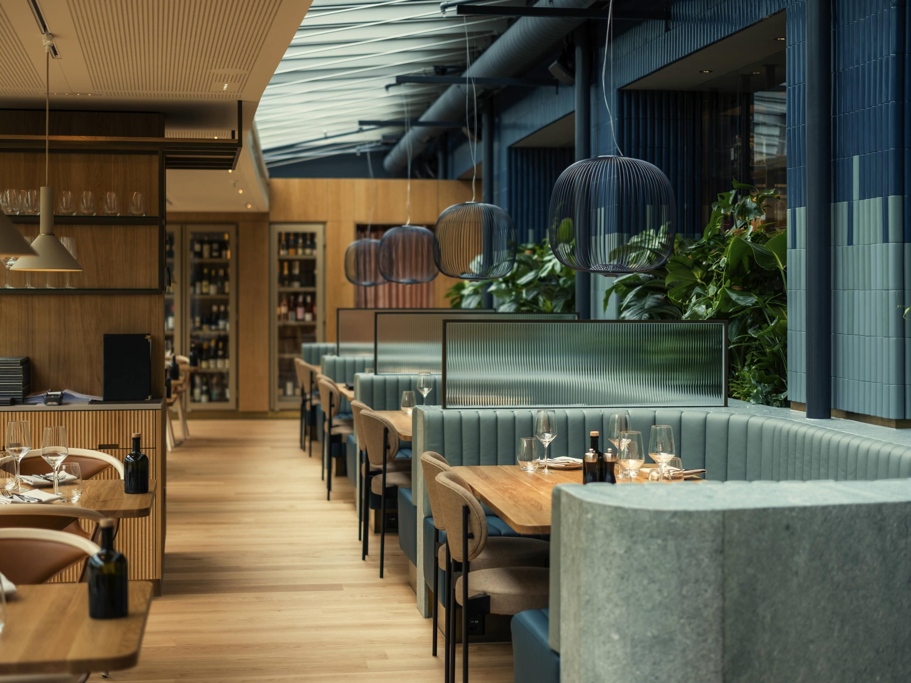 A modern restaurant with wooden flooring, blue upholstered seating, and hanging pendant lights.