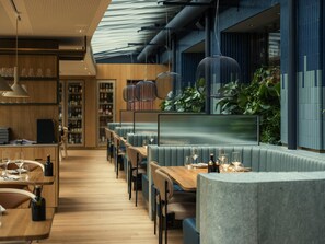 A modern restaurant with wooden flooring, blue upholstered seating, and hanging pendant lights. - Swissôtel Kursaal Bern (Bern)