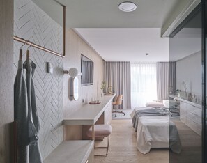 Una habitación de hotel moderna con una pared de diseño en patrón de espiga, un tocador de madera, un espejo grande, un escritorio con una silla, una cama y un panel de vidrio.