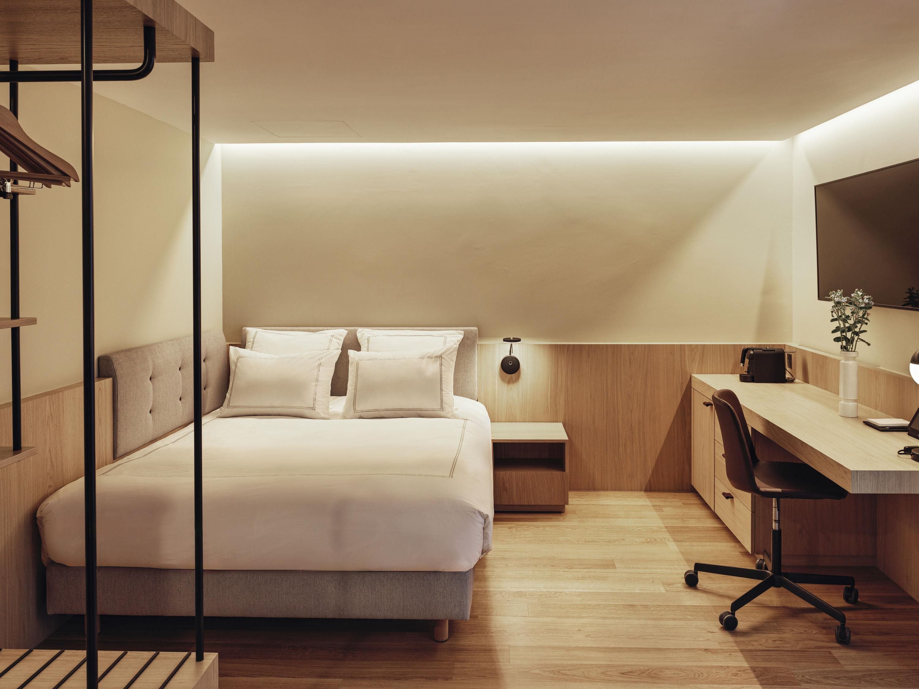 A modern bedroom with a bed, bedside table, desk, chair, and a skylight.