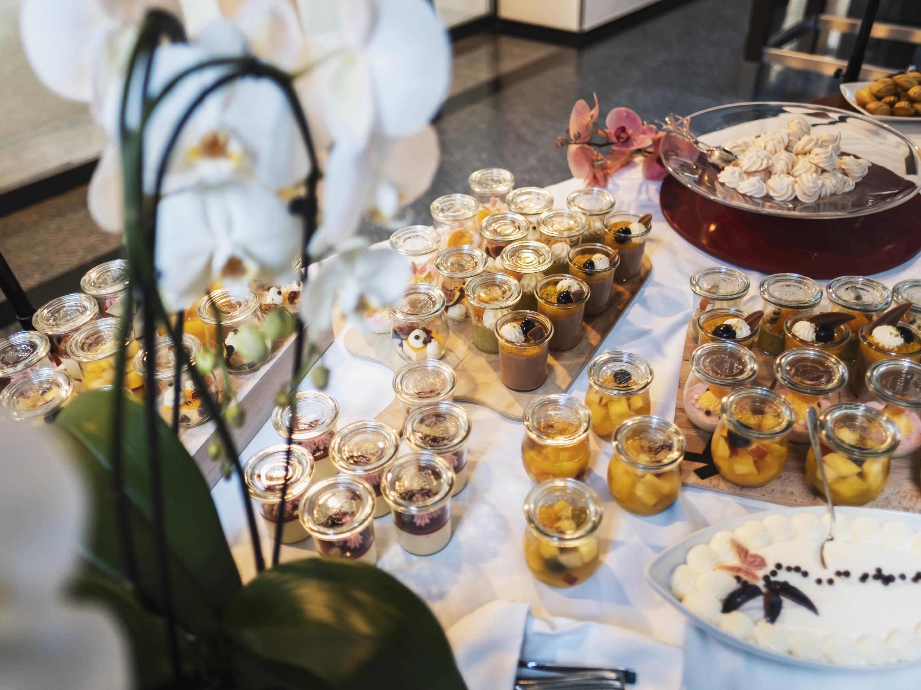 Une table sur laquelle on trouve divers aliments, notamment des pots de confitures et des desserts.