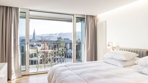 A bedroom with a large bed, a view of a cityscape through a sliding glass door, and a balcony with chairs. - Swissôtel Kursaal Bern (Bern)