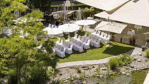 An outdoor seating area with white chairs and umbrellas, surrounded by greenery and a small pond. - Swissôtel Kursaal Bern (Bern)