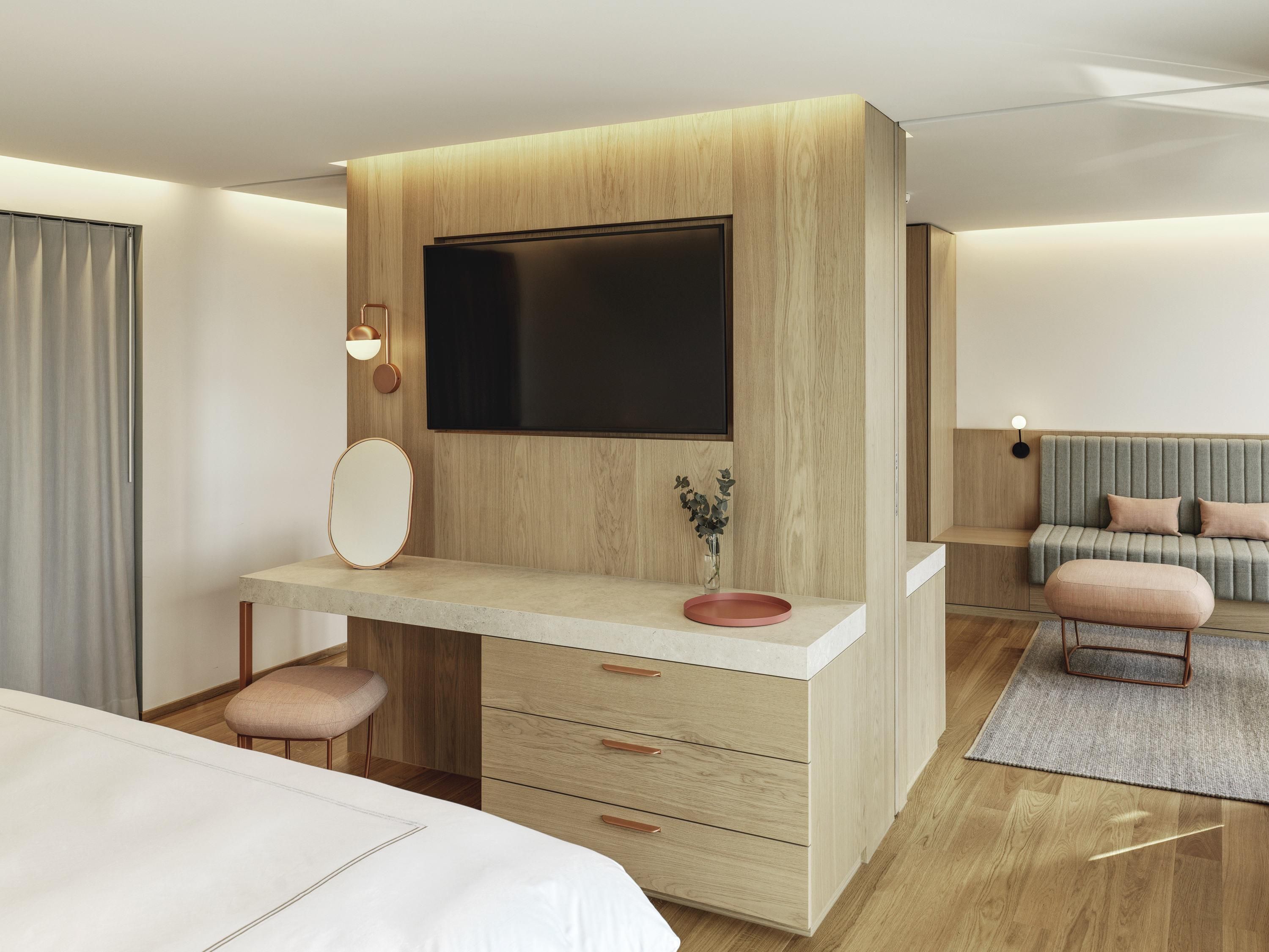 Une chambre d’hôtel moderne avec un mur d’accent en bois, une grande télévision à écran plat, une coiffeuse avec un miroir et un canapé.
