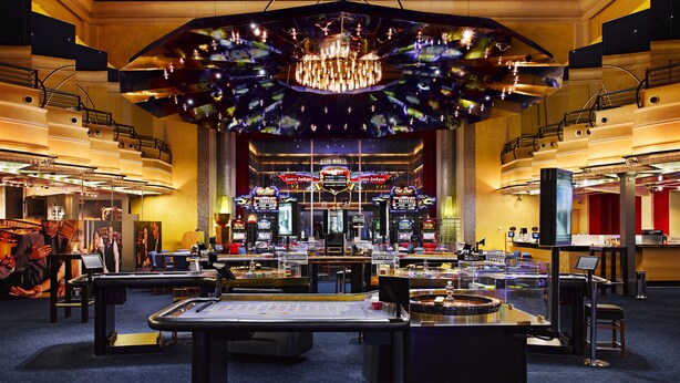 A spacious casino with multiple gaming tables and a large chandelier.