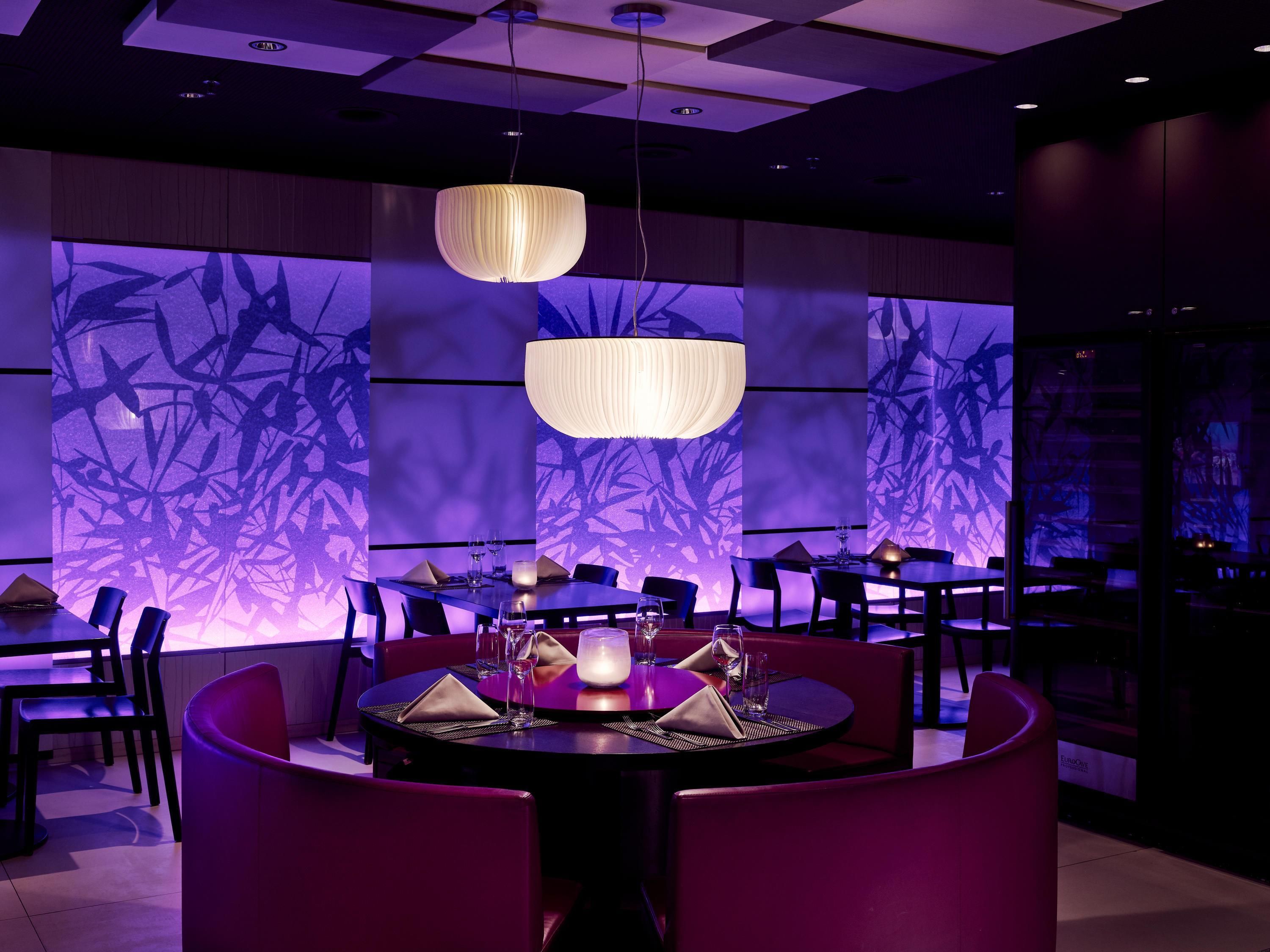 A modern dining area with round tables, black chairs, and ambient lighting.
