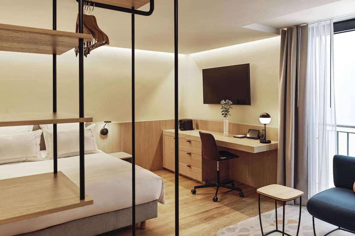 Ein Hotelzimmer mit Etagenbett, Schreibtisch mit Stuhl, kleinem Tisch, Wand-Fernseher und einem Fenster mit Vorhängen.
