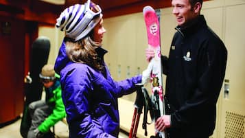 A person holding skis in a room with wooden paneling and a door in the background.