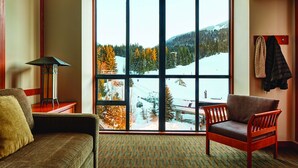 Una habitación con un ventanal que ofrece vistas a un paisaje nevado, un sofá, una silla y una lámpara.