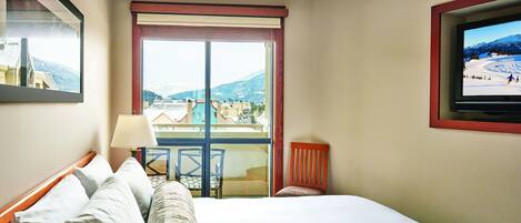 A hotel room with a large bed, a television mounted on the wall, a window with a view of a snowy landscape, and a chair by the window.