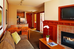 A living room with a fireplace, a dining area, and a kitchen in the background.