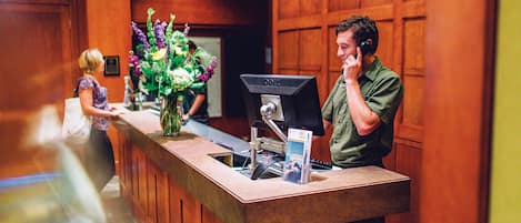 A reception desk with a computer monitor, a vase of flowers, and a framed certificate on the wall.