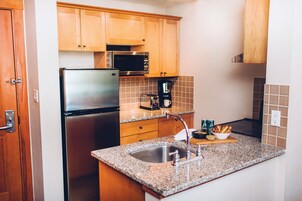 Una cocina con armarios de madera, un refrigerador de acero inoxidable, un microondas, una cafetera y una encimera de granito.