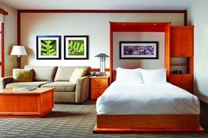 Una habitación de hotel con una cama, un sofá, una mesita de noche, una lámpara y cuadros en la pared.