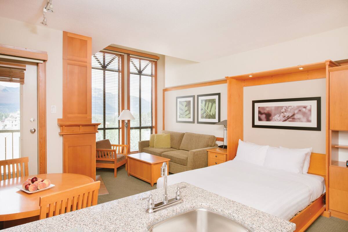 Una habitación de hotel con cama, escritorio, sillón, sofá y ventana con persianas.