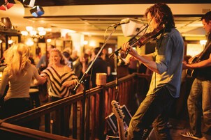 A musician performing on stage with a microphone stand and an audience in the background.