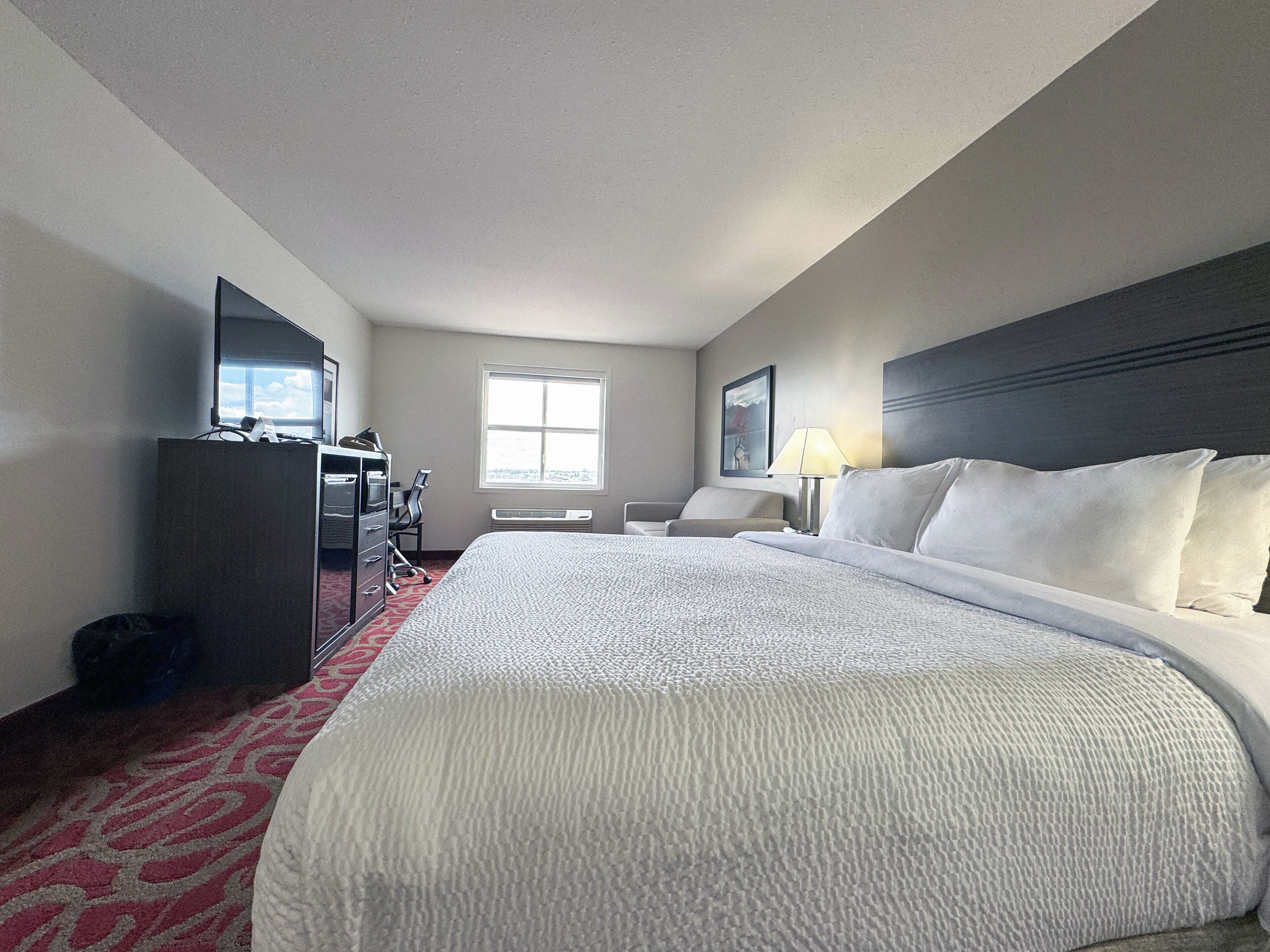 A hotel room with a large bed, a desk with a chair, a TV, and a window with a view.
