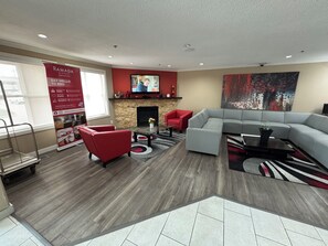 Een moderne woonkamer met een modulaire bank, rode fauteuils, een open haard en een groot abstract schilderij.