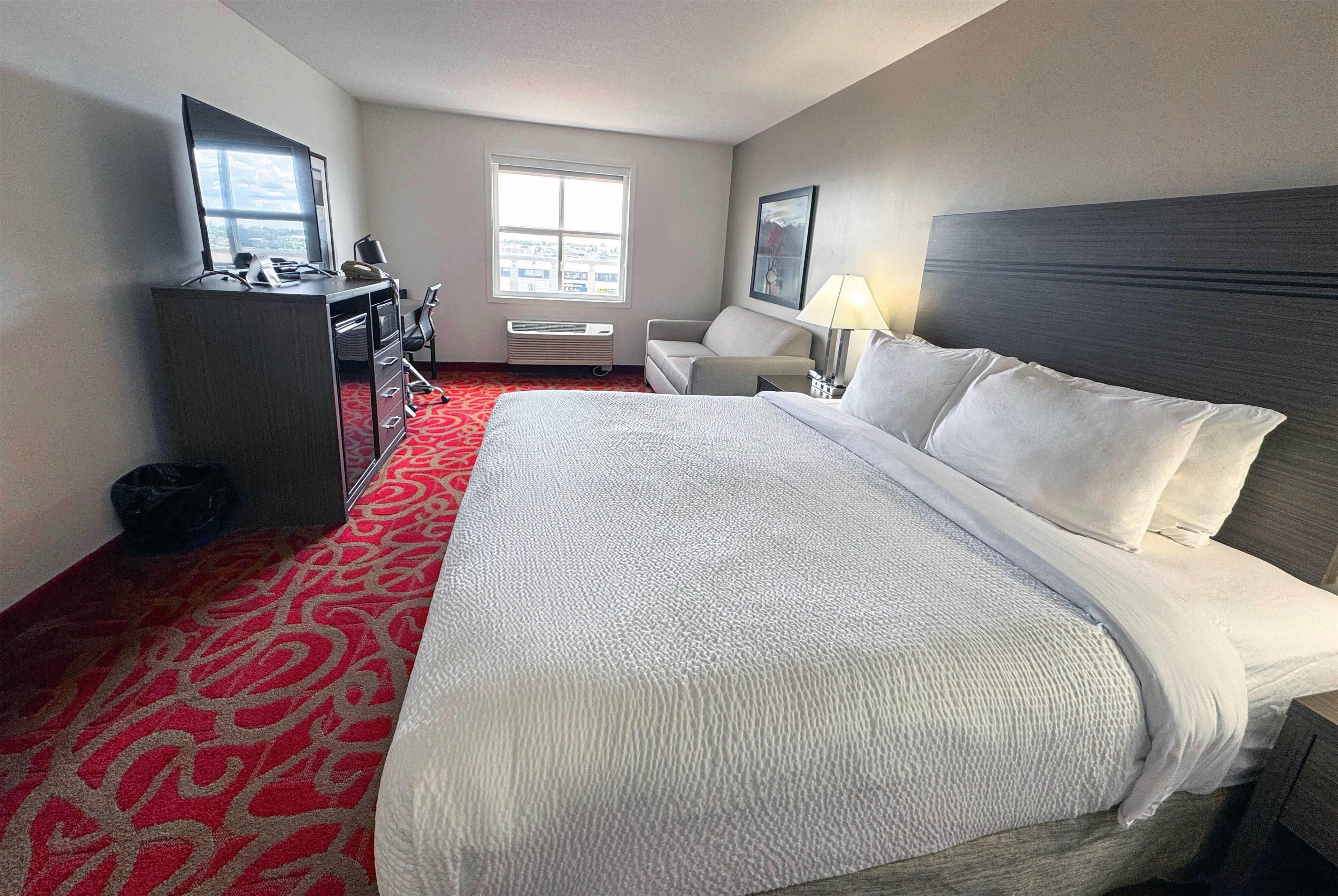 A hotel room with a large bed, a desk with a computer, a chair, a window, and a lamp.