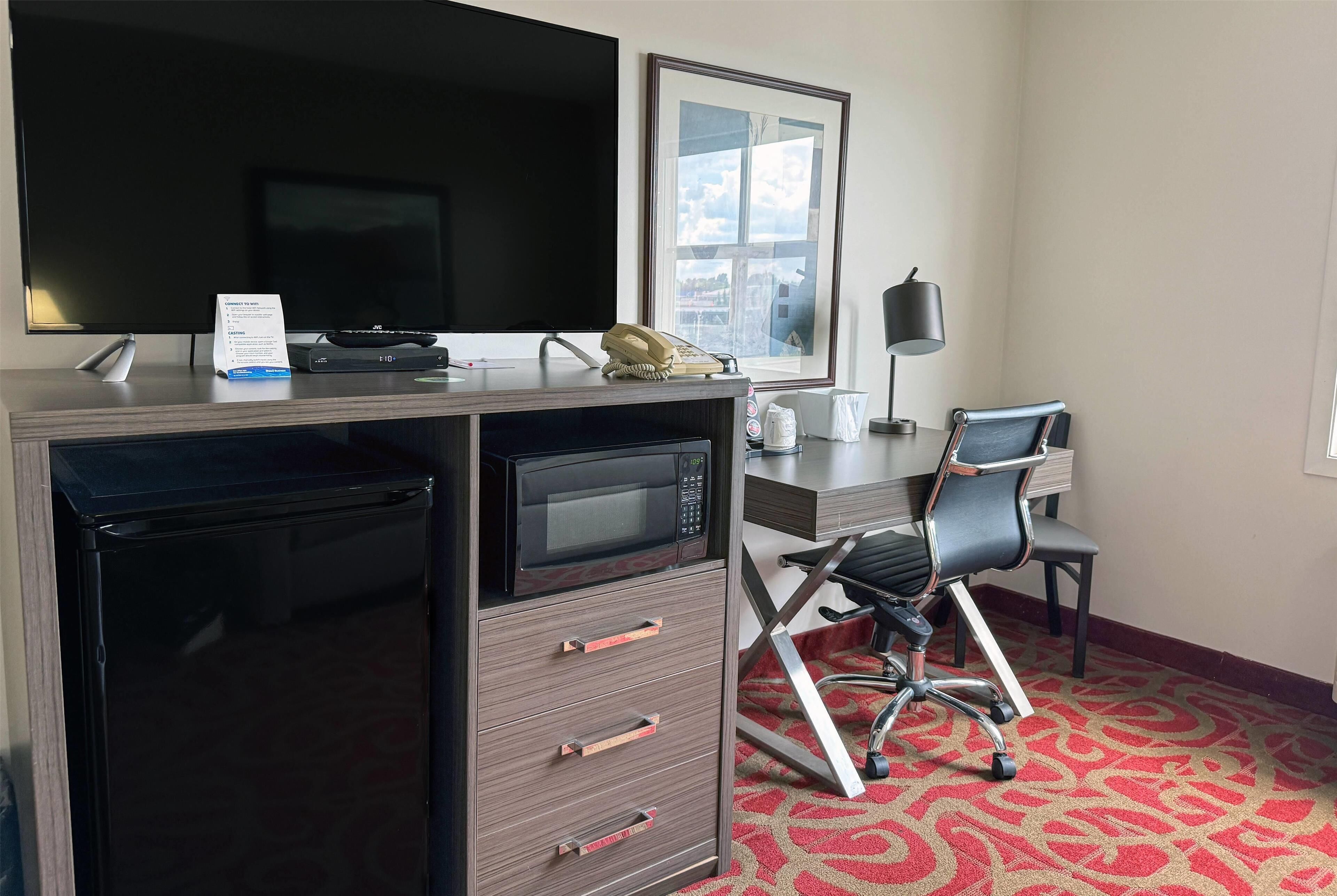 Une chambre d’hôtel équipée d’un bureau, d’une télévision, d’un four à micro-ondes, d’un téléphone, d’une chaise et d’une fenêtre donnant sur un paysage agréable.