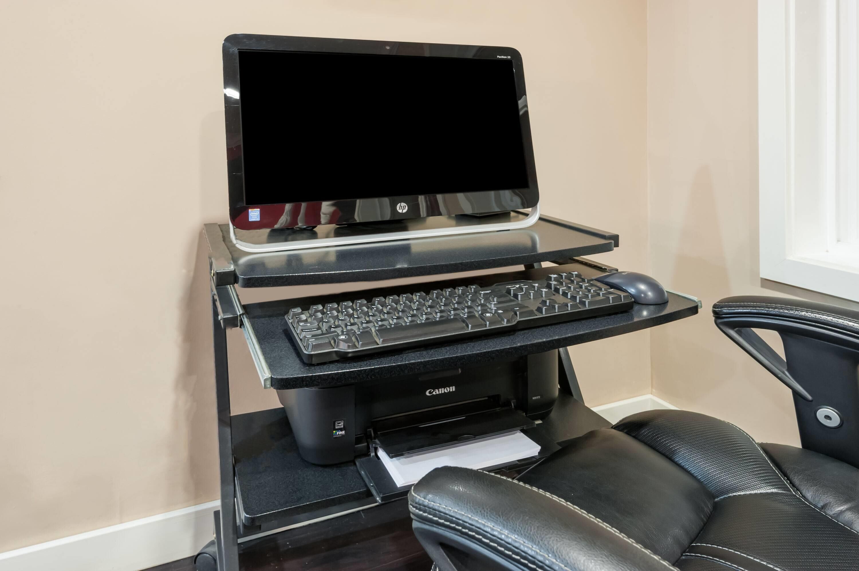A desktop computer setup with a monitor, keyboard, and mouse on a stand, along with a printer and a leather chair.