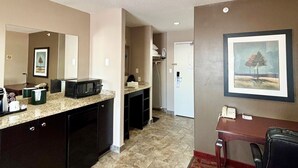 Cocina moderna con encimeras de granito, microondas y fregadero. Cuenta con una zona de comedor con mesa y sillas, y suelo alfombrado.