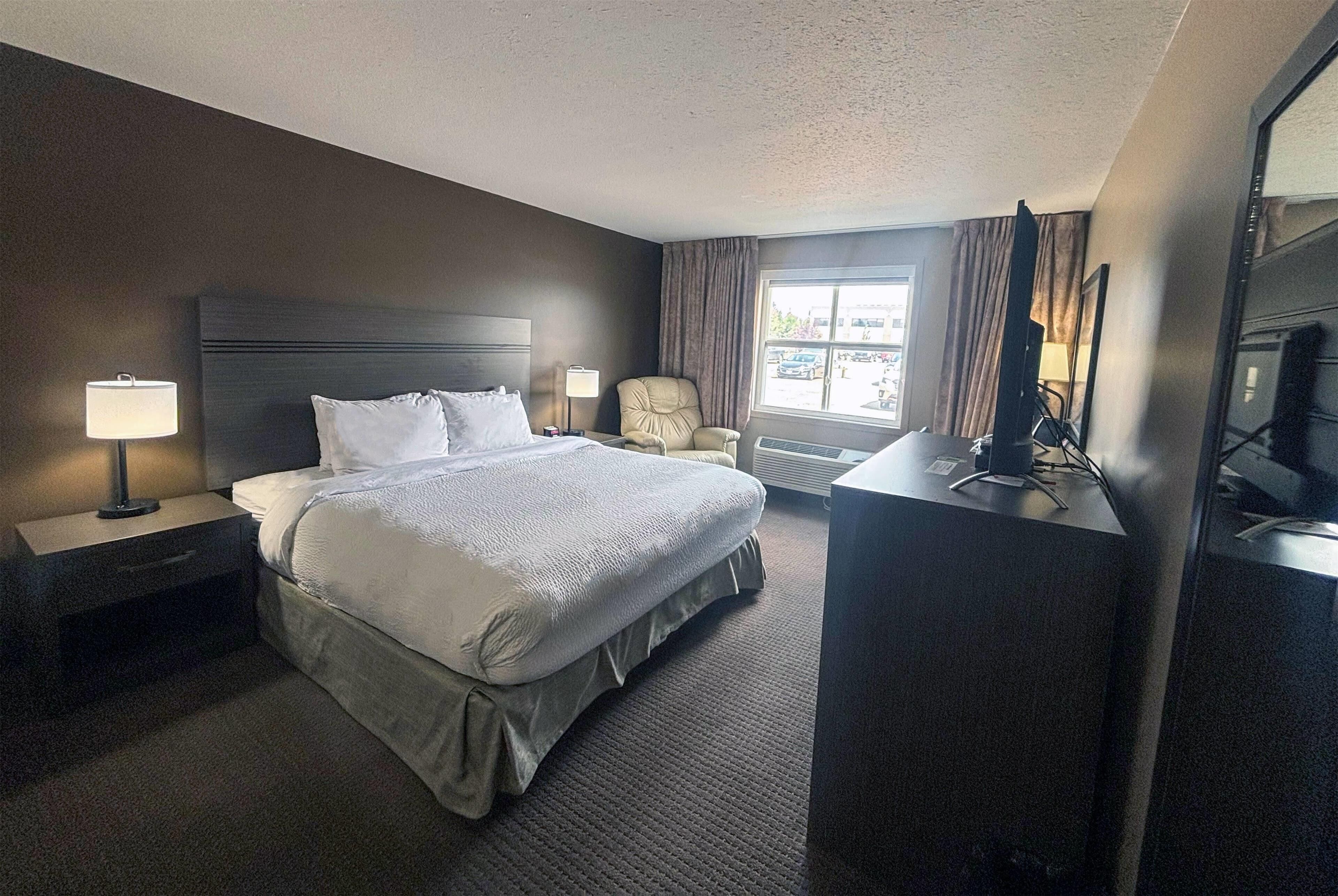 A hotel room with a large bed, a desk with a computer, a chair, and a window with curtains.