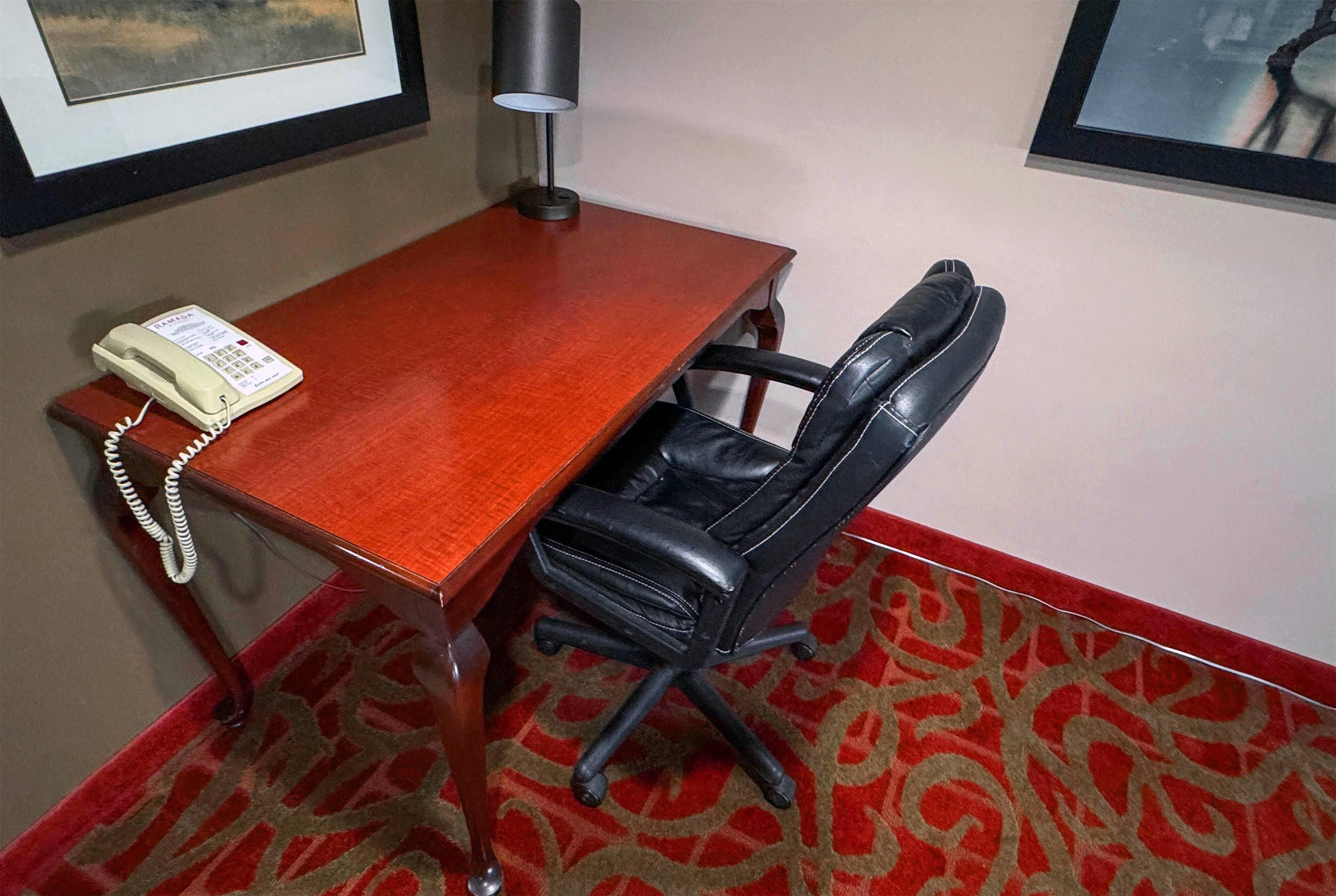 Une chambre d’hôtel avec un bureau en bois, un fauteuil en cuir noir, un téléphone et une moquette à motifs.