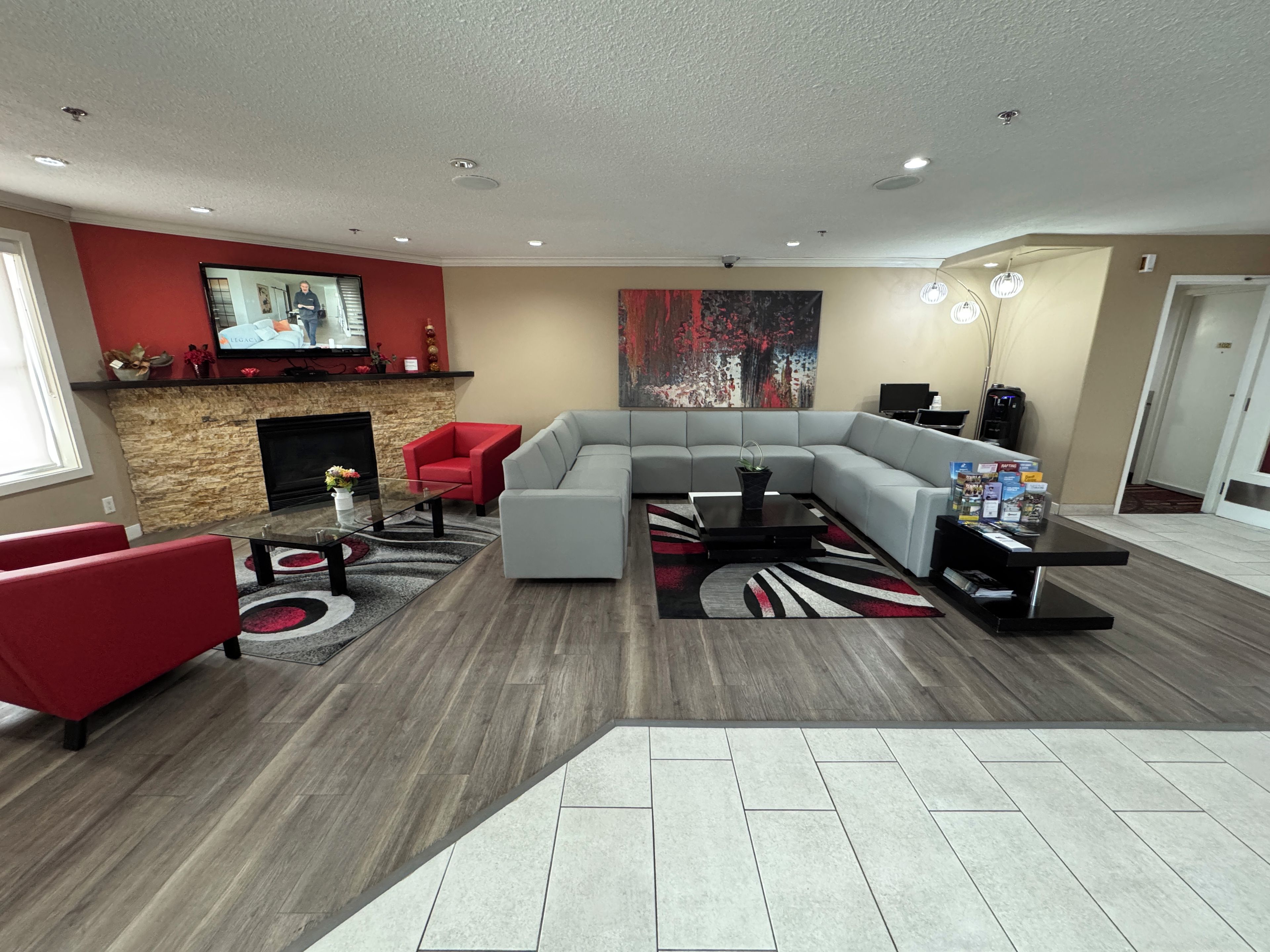 A modern living room with a sectional sofa, red armchairs, a fireplace, a flat-screen TV, and a large abstract painting.