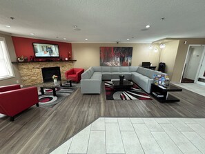 Een moderne woonkamer met een modulaire bank, rode fauteuils, een open haard, een flatscreen televisie en een groot abstract schilderij.
