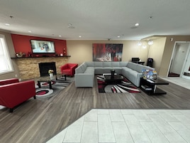 A modern living room with a sectional sofa, red armchairs, a fireplace, a flat-screen TV, and a large abstract painting.