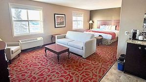 Habitación de hotel con alfombra roja estampada, sofá blanco, cama con cabecera roja, una mesita y un radiador.