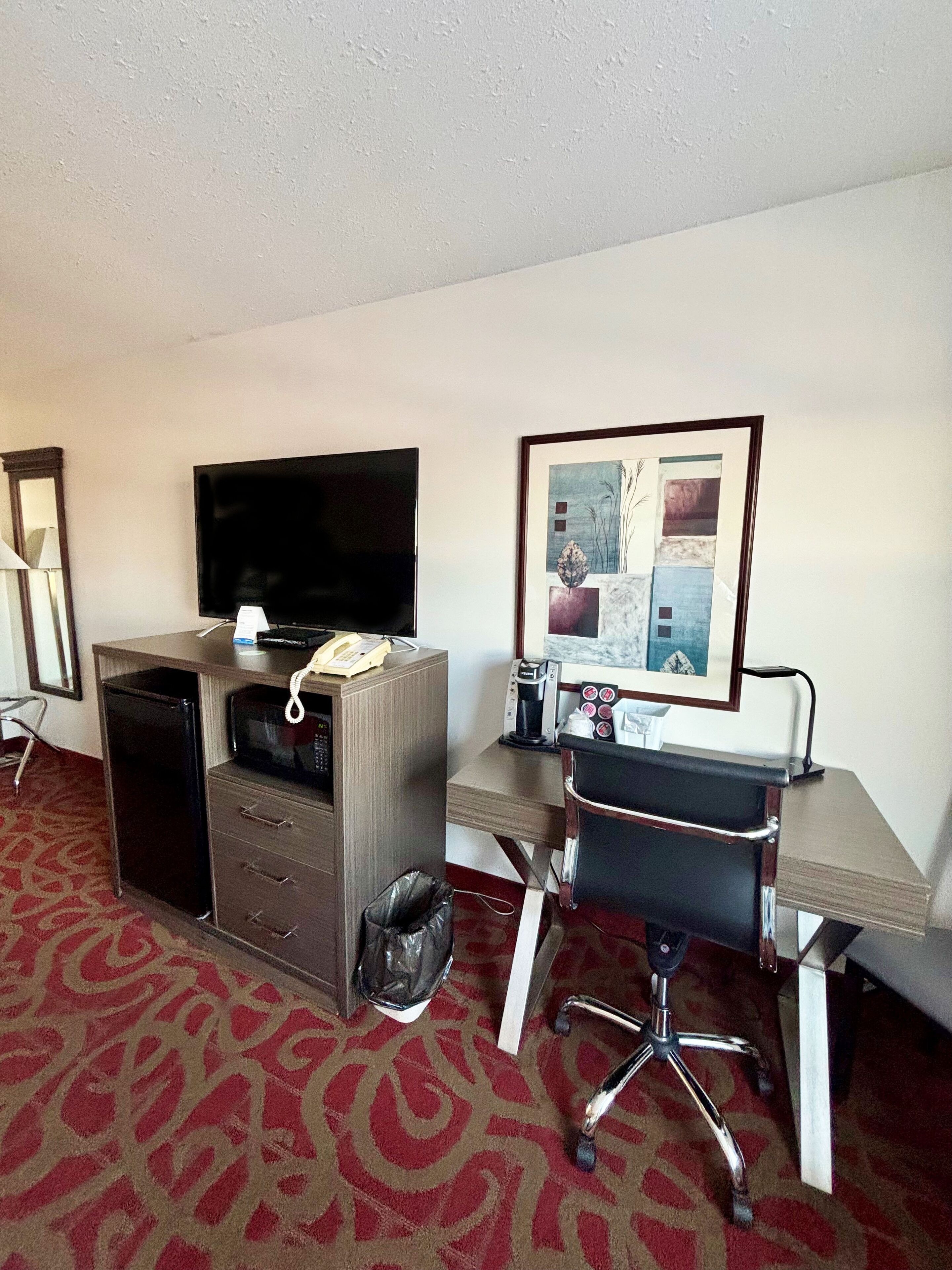 A hotel room with a desk, chair, television, and a framed picture on the wall.