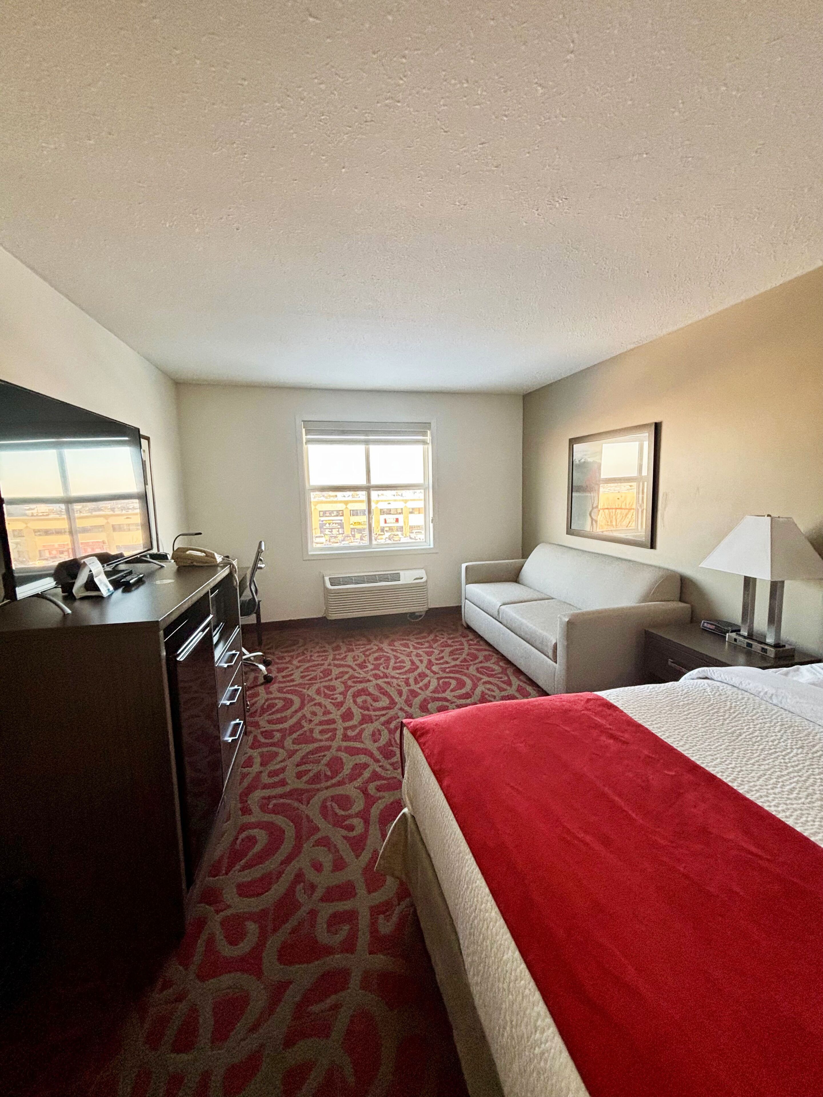 A hotel room with a bed, a desk, a chair, a sofa, and a window.