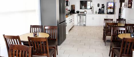 A modern kitchen with white cabinets, a stainless steel refrigerator, and a dining area with wooden chairs and tables.