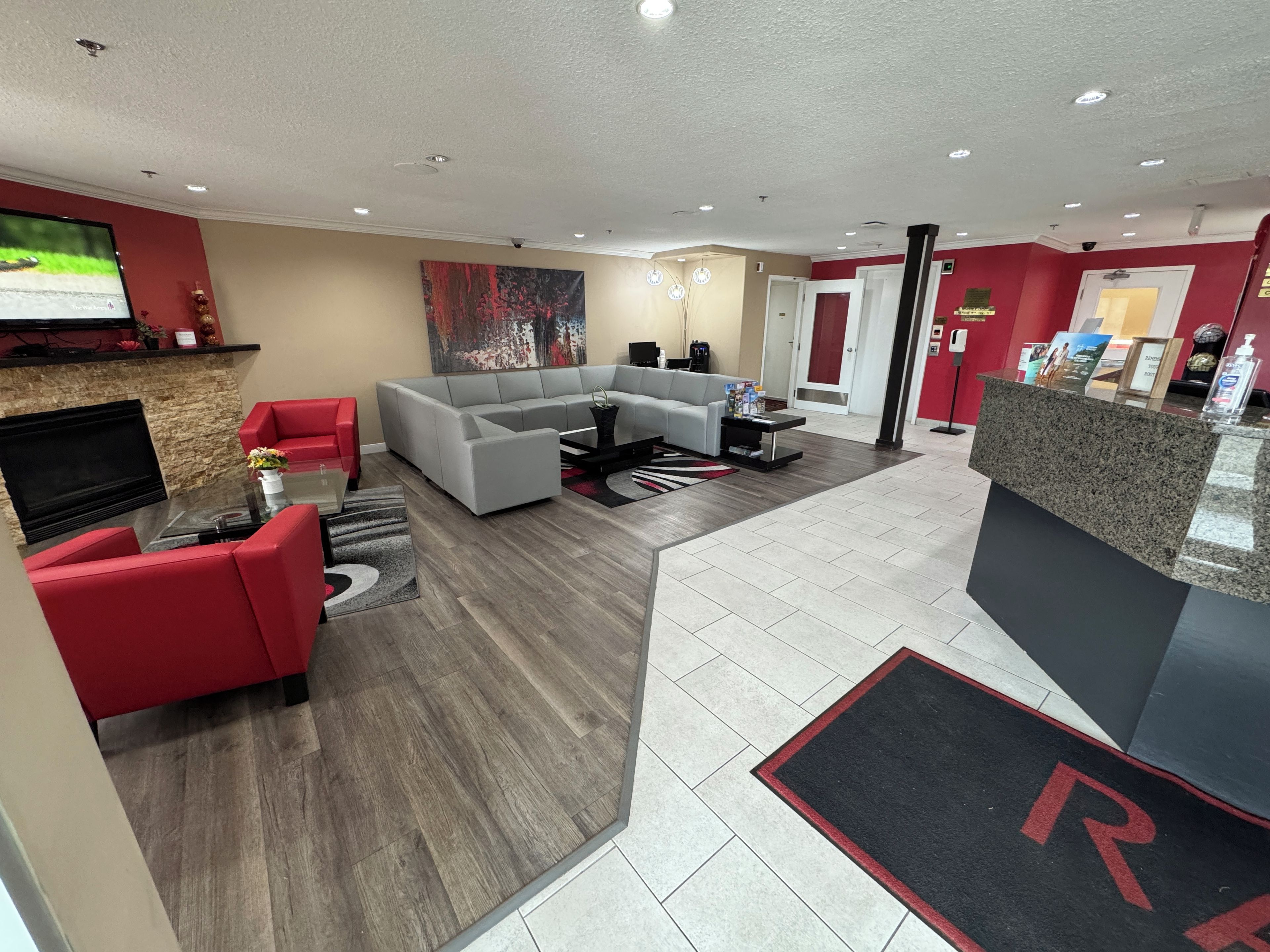 Un lobby moderno con un sofá seccional gris, sillones rojos, un televisor de pantalla plana y un mostrador de recepción.