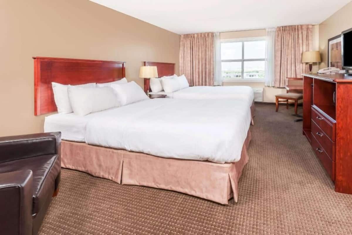 Une chambre d’hôtel avec deux lits, un bureau, une chaise, une télévision et une fenêtre avec des rideaux.