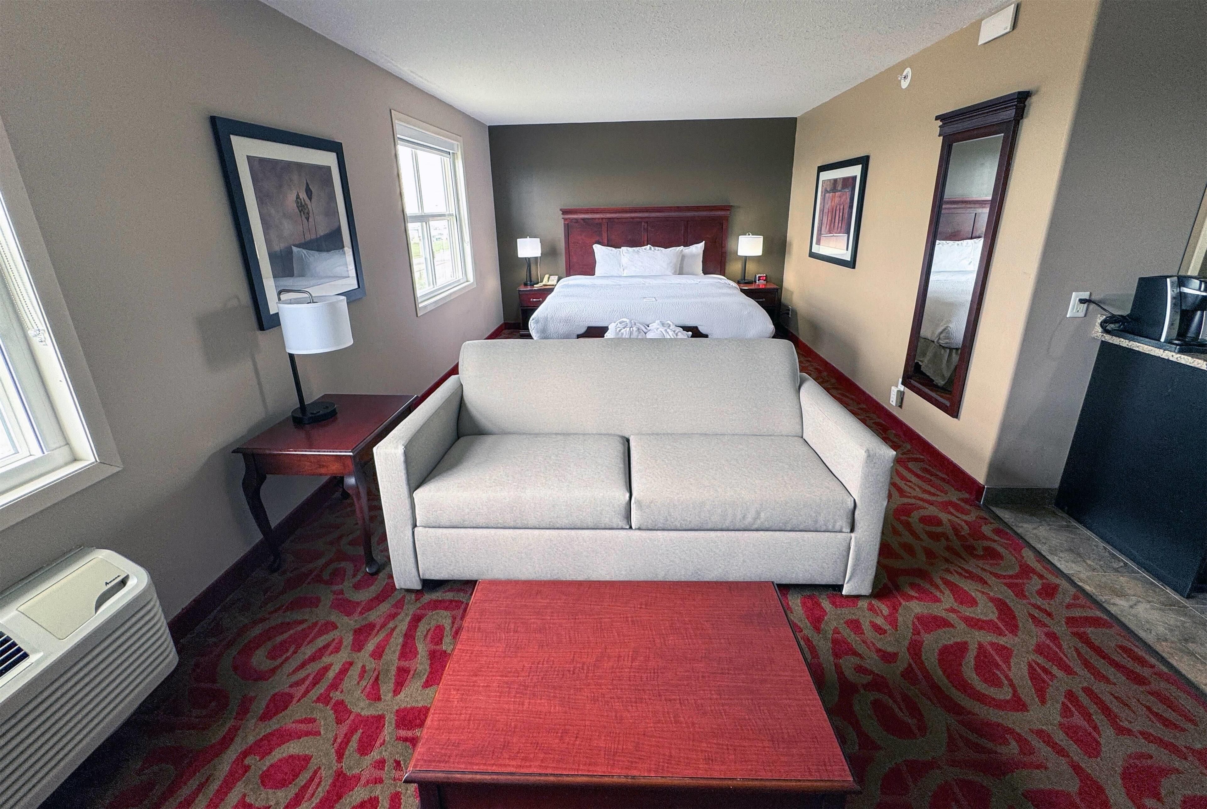 Habitación de hotel con cama, sofá, mesita, lámpara, espejo y calefactor.
