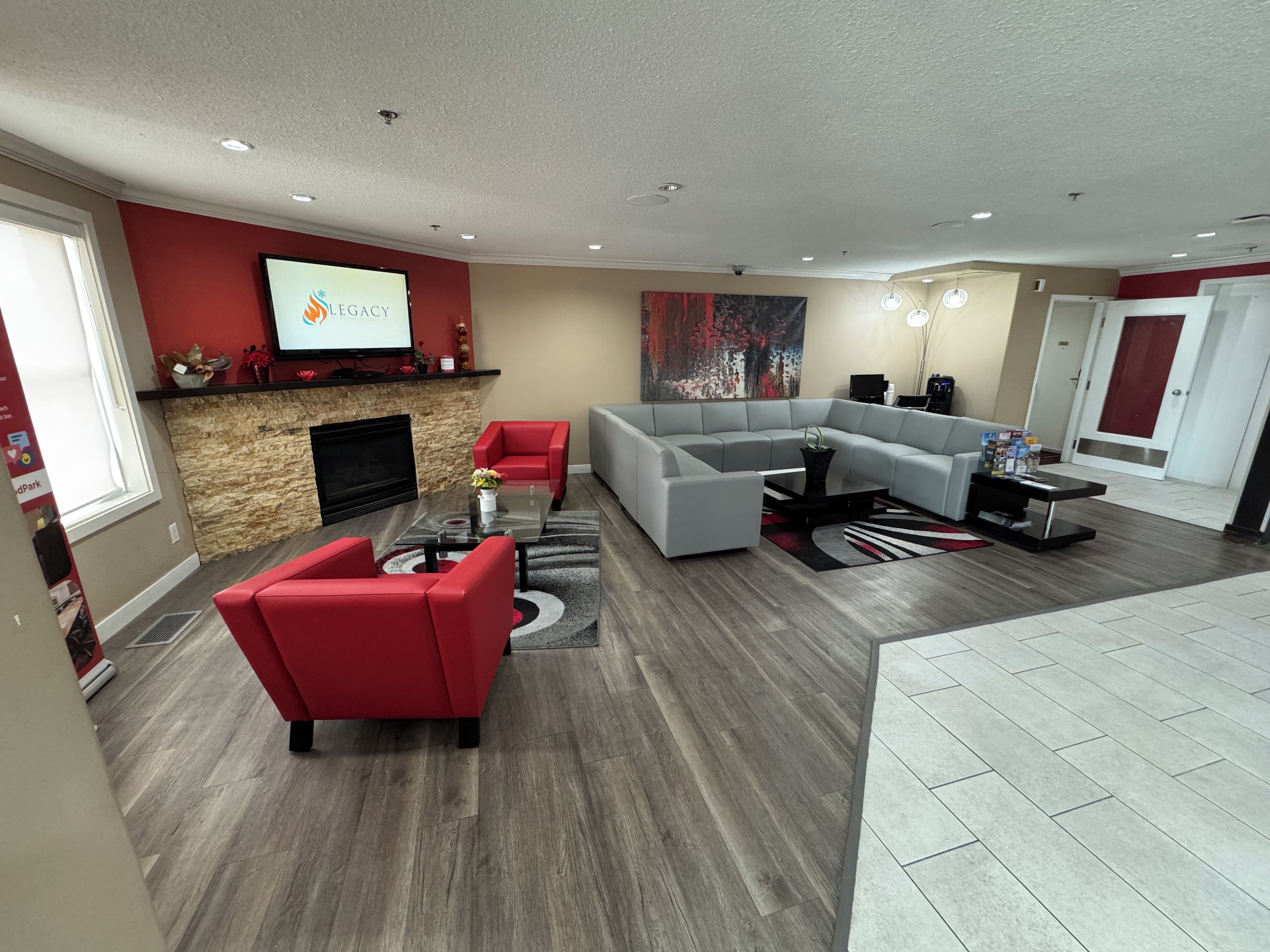 A modern living room with a fireplace, red and grey sofas, a large sectional sofa, and a flat-screen TV mounted on the wall.