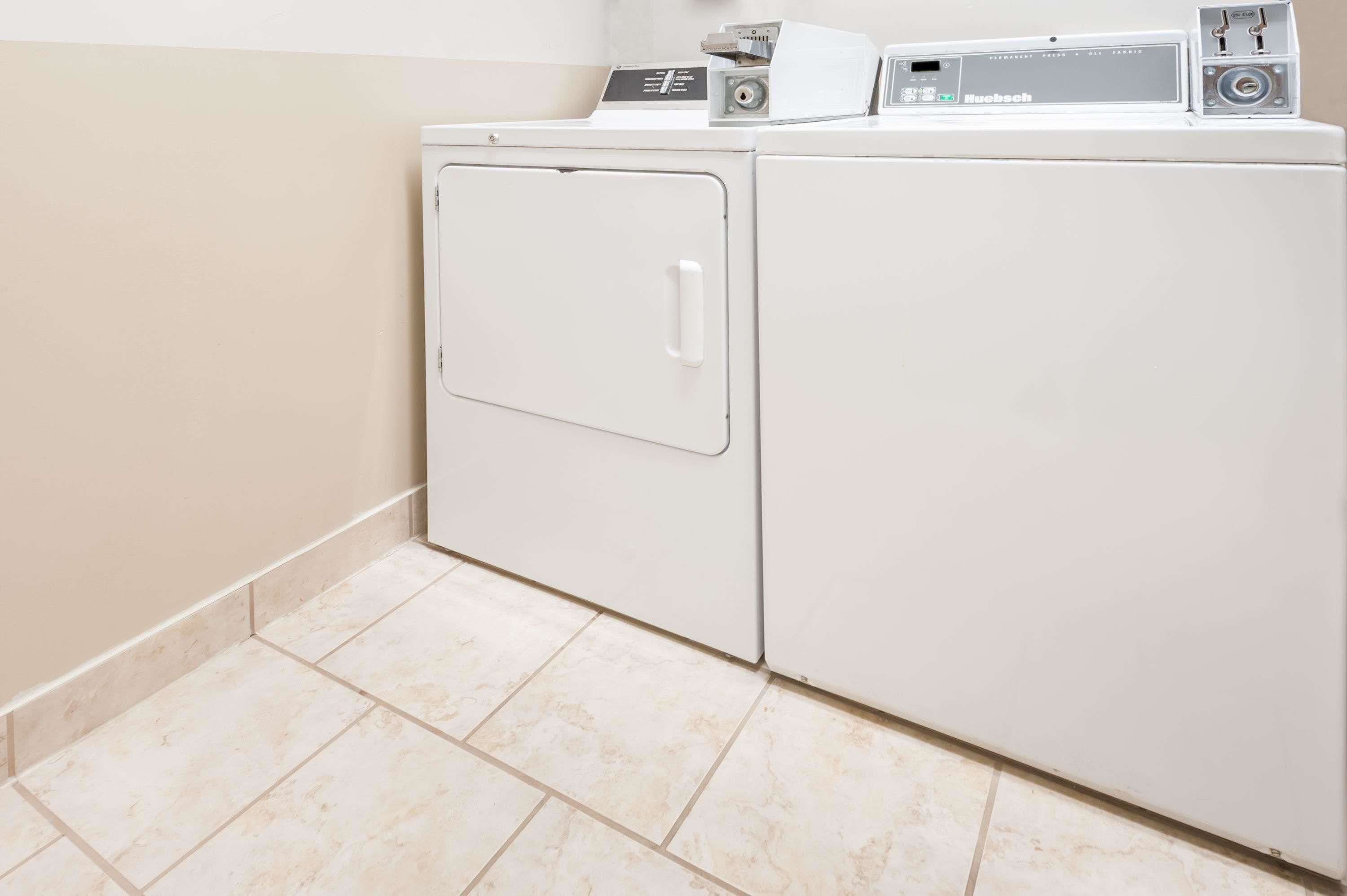 Un lavadero moderno con lavadora y secadora de carga frontal, un panel de control y piso de baldosas.