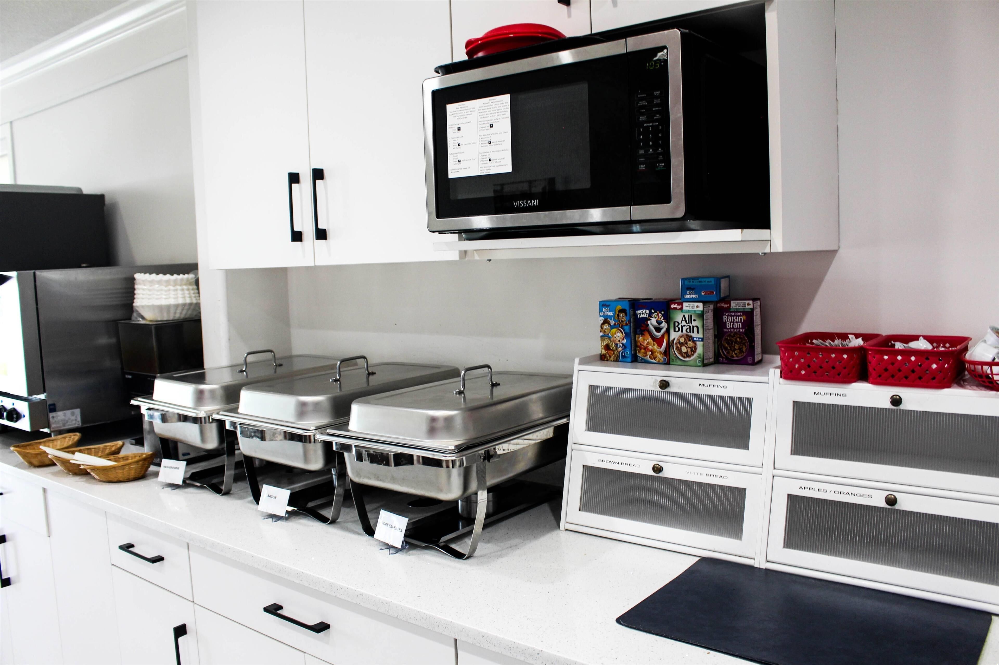 Een keuken met roestvrijstalen apparatuur, waaronder een magnetron en een koelkast. Er zijn cateringpunten met voorzien schaaltjes en manden.