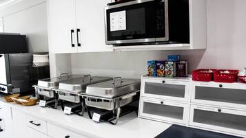 Een keuken met roestvrijstalen apparatuur, waaronder een magnetron en een koelkast. Er zijn cateringpunten met voorzien schaaltjes en manden.