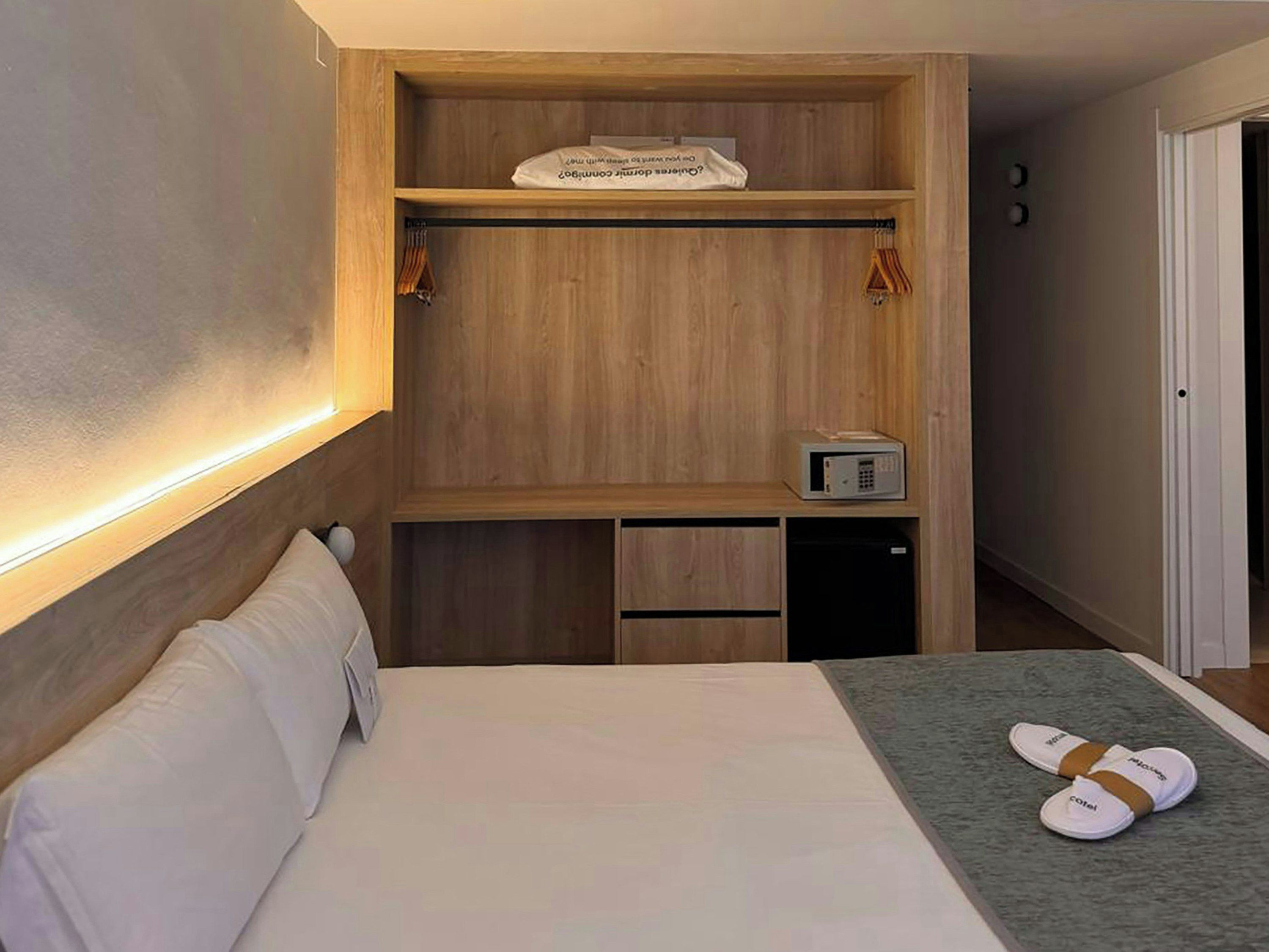 Une chambre d’hôtel avec un lit, une armoire en bois, un four à micro-ondes et des chaussons sur le lit.