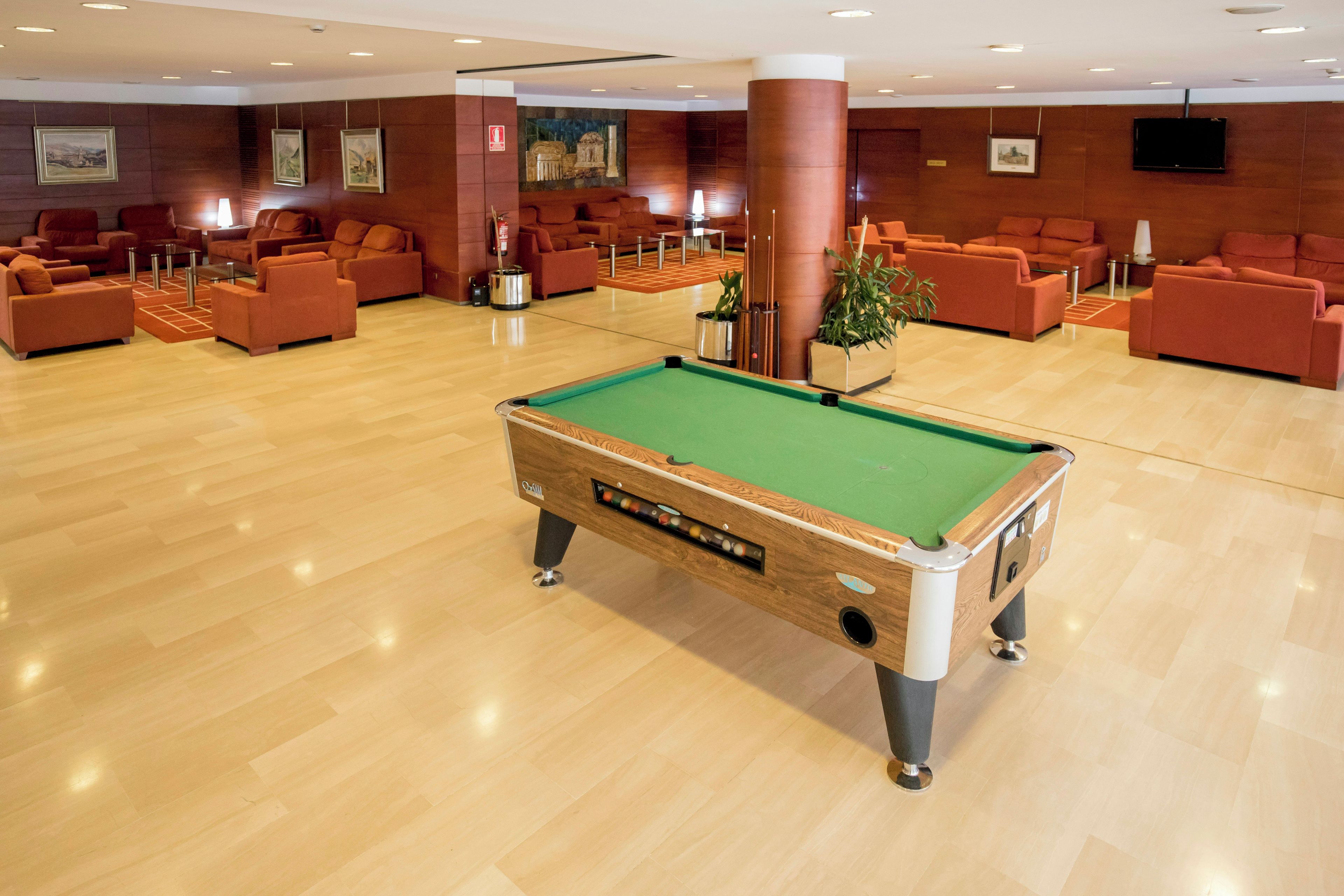 A pool table in a spacious room with multiple seating areas and a television mounted on the wall.