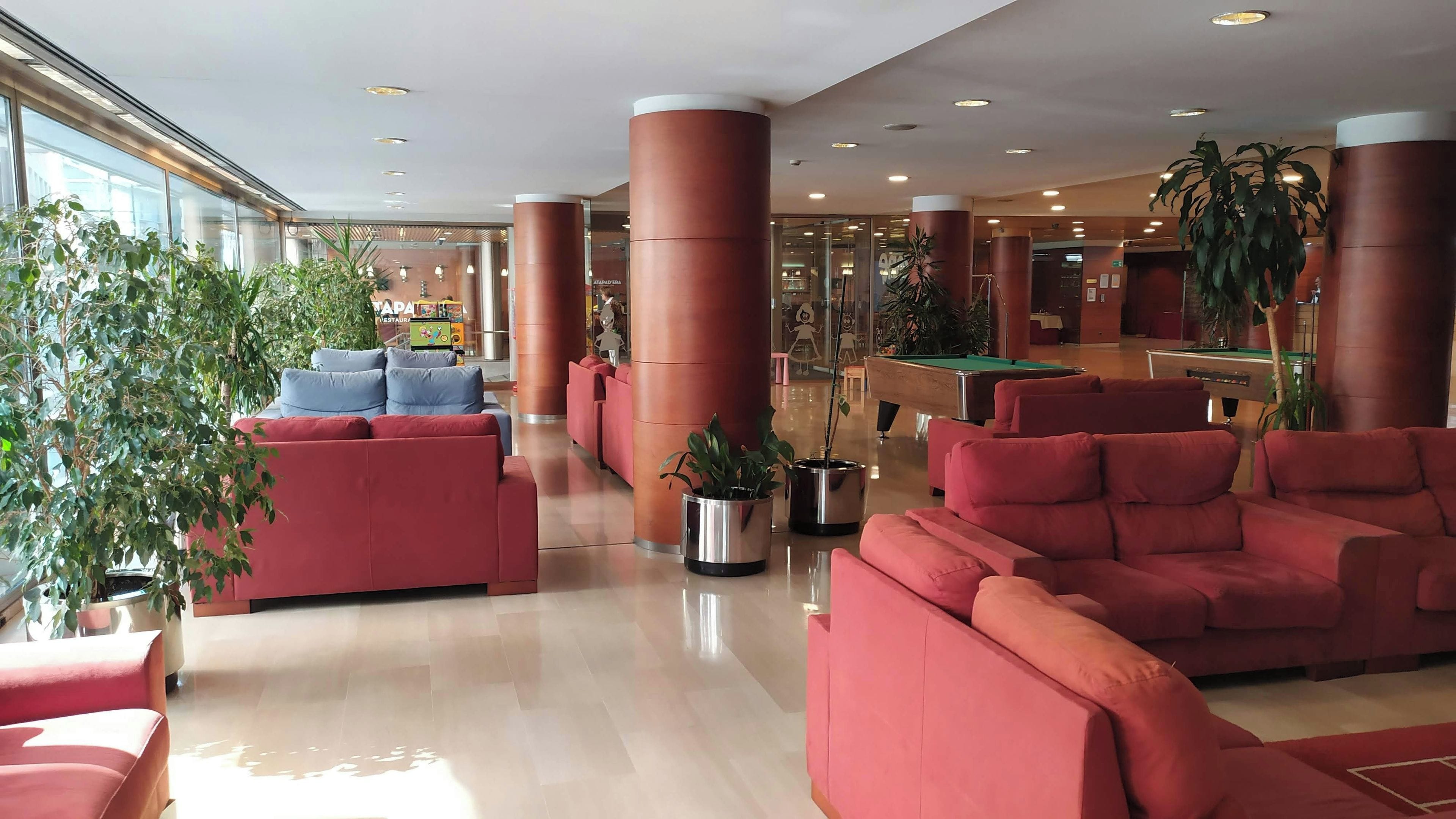 A spacious lobby with red sofas, a pool table, and potted plants.