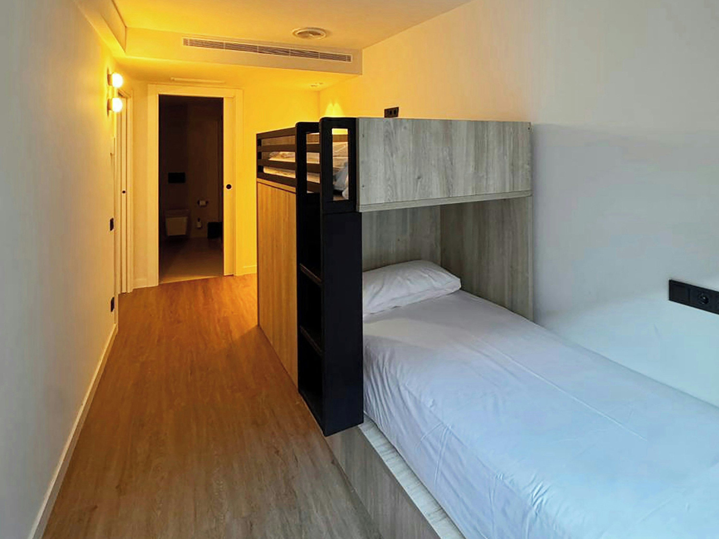 Una habitación con literas, suelo de madera y una puerta que da a otra estancia.