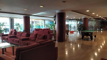 Un vestíbulo amplio con asientos rojos, mesa de billar y grandes ventanales que dejan entrar luz natural.