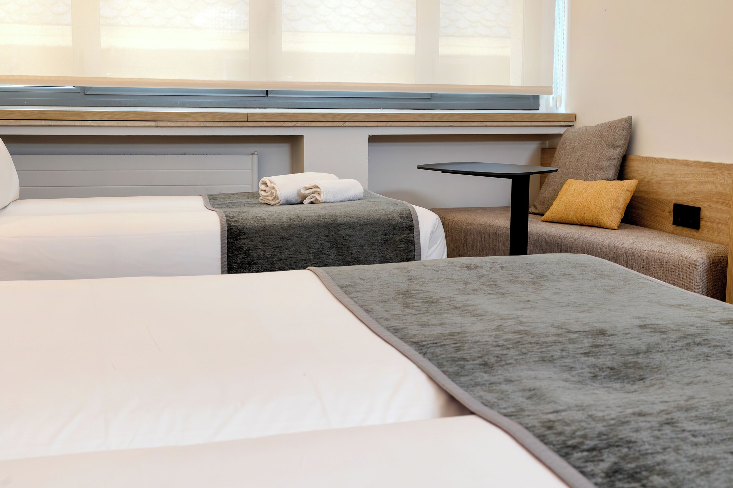 Habitación de hotel con dos camas, una mesita y un banco.