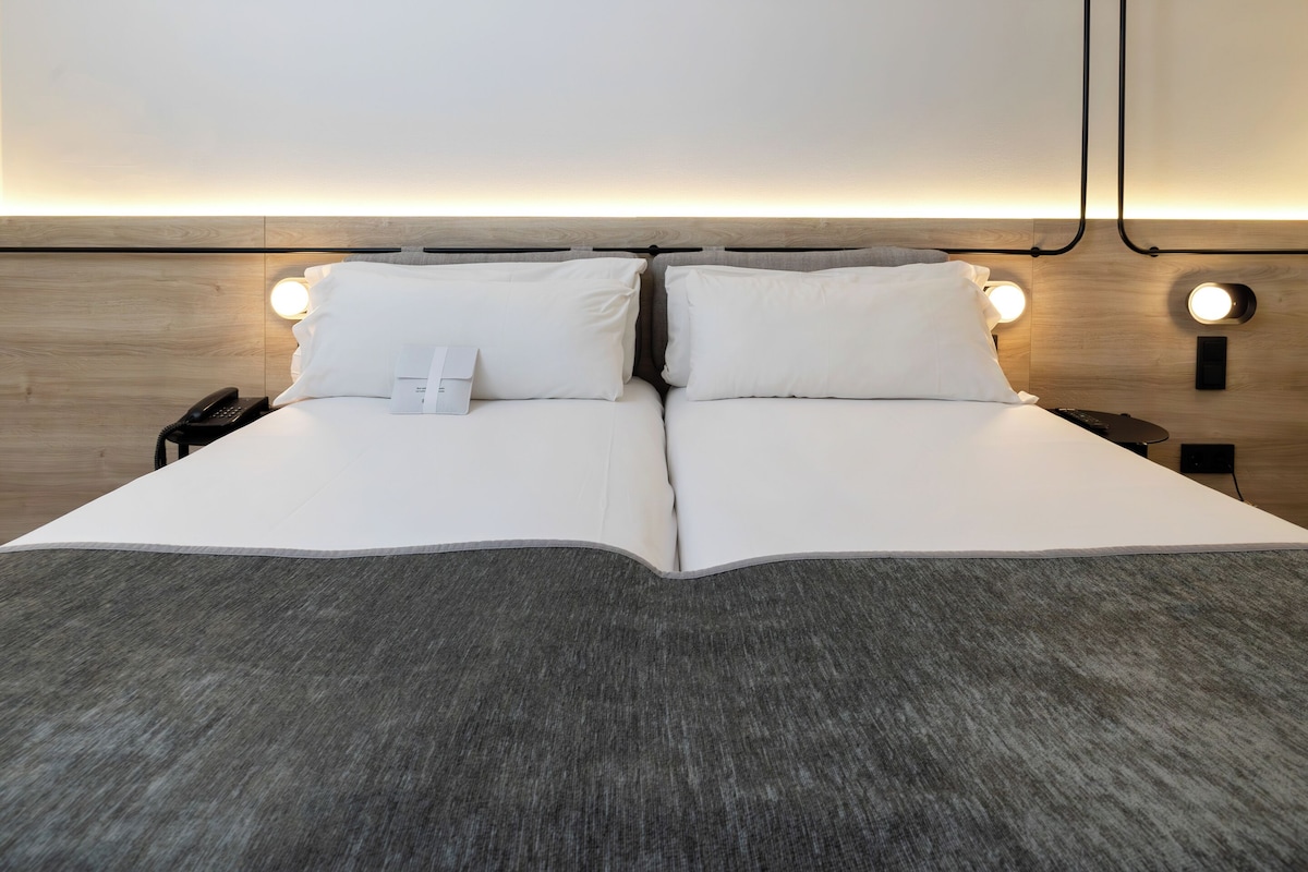 A double bed with white linens, a bedside phone, and two wall-mounted reading lights.